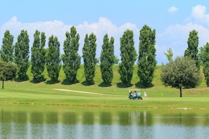 A golf course with a pond, trees, and a golf cart.