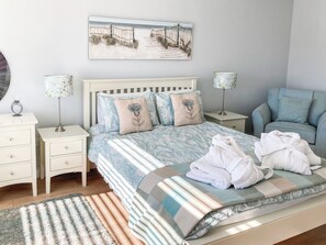 A bedroom with a bed, two bedside tables, a chair, a rug, and a wall-mounted picture.