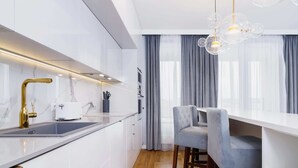 A modern kitchen with white cabinetry, a gold faucet, and a bar stool. - Stylish Apartment with 2 Bedrooms | Parking and Balcony (Kraków)