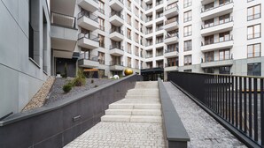 A modern multi-story building with a central staircase leading to a covered entrance. - Stylish Apartment with 2 Bedrooms | Parking and Balcony (Kraków)