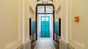 Un couloir avec un sol à motifs, une porte turquoise au fond et un détecteur d’incendie sur le mur.