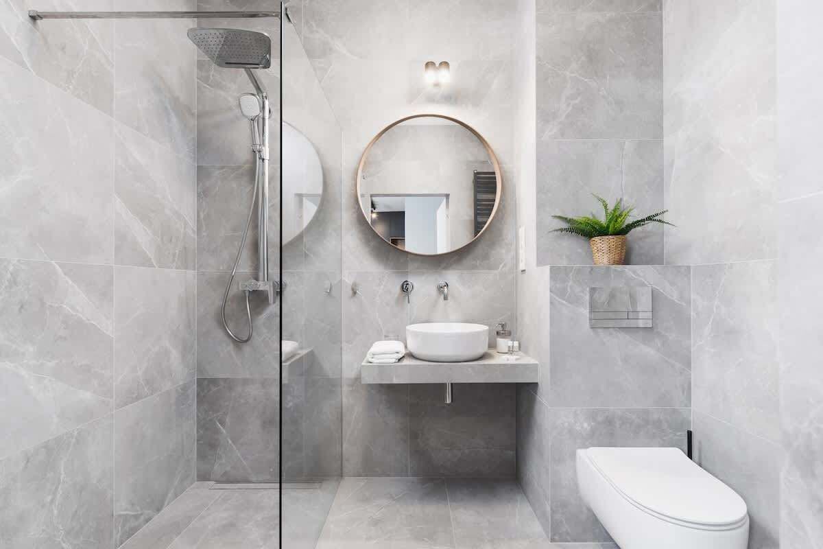 Een moderne badkamer met een douchecabine van glas, een ronde spiegel, een wastafel en een toilet.