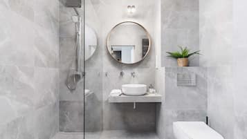 Een moderne badkamer met een douchecabine van glas, een ronde spiegel, een wastafel en een toilet.