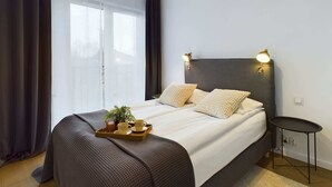 Quarto moderno com uma cama grande, duas luminárias de cabeceira, uma mesinha e uma janela com cortinas.