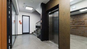 Um elevador moderno com acabamento metálico, escadas com guarda-corpos pretos e parede com padrão de tijolos.