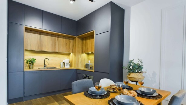 Cozinha moderna com armários escuros, bancada de madeira e uma mesa de jantar posta com pratos, copos e uma planta.