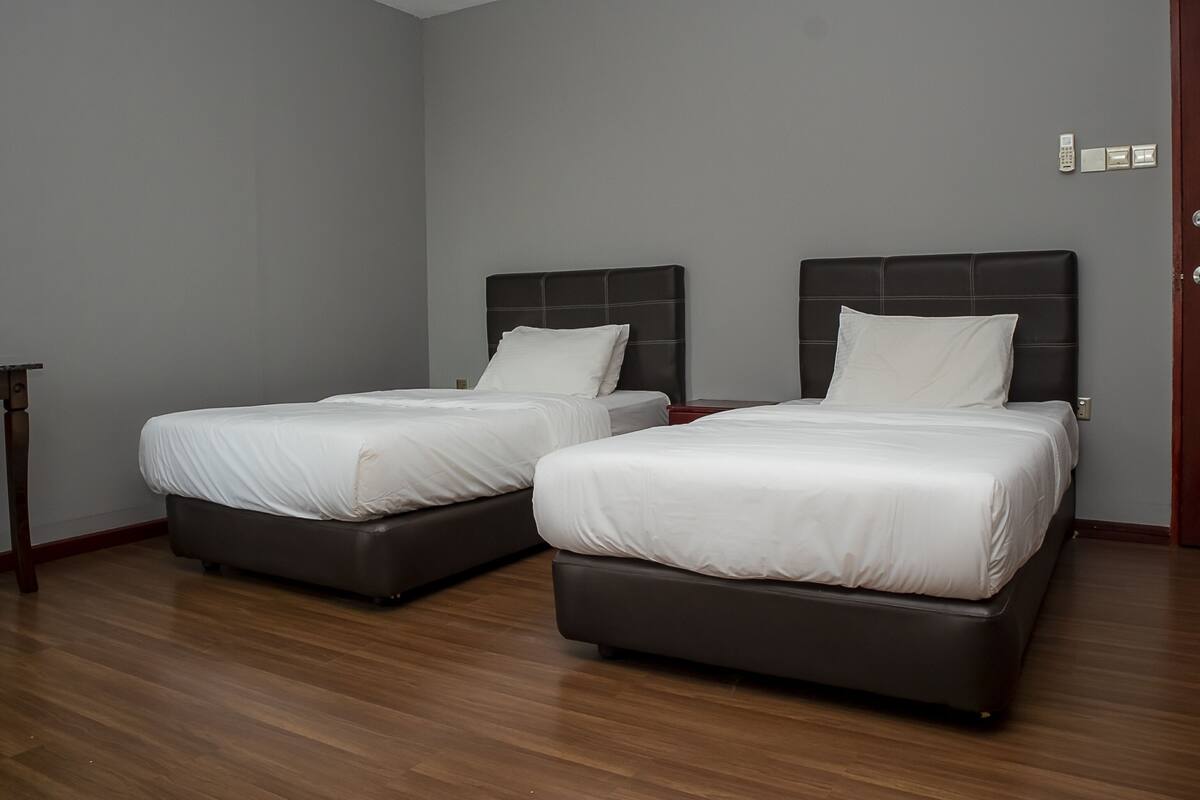 A hotel room with two beds, wooden flooring, and a door.