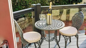 Ein Metalltisch mit zwei Stühlen und einer Champagnerflasche auf einem Holzboden.