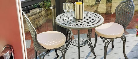 Ein Metalltisch mit zwei Stühlen und einer Champagnerflasche auf einem Holzboden.