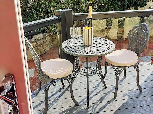 A metal table with two chairs and a bottle of champagne on a wooden deck.