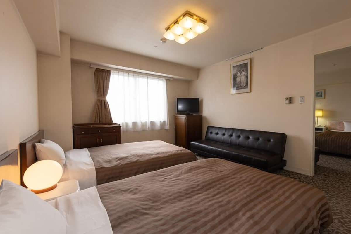 A hotel room with two beds, a TV, a sofa, and a large window with curtains.