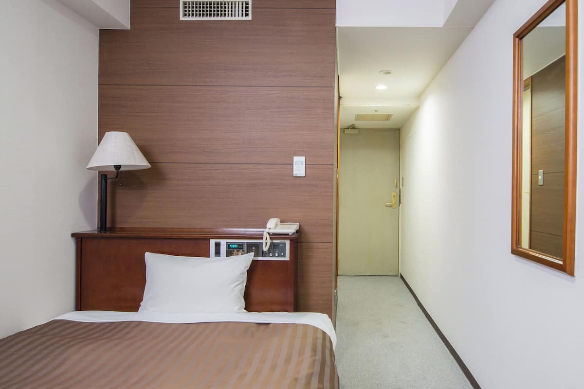 Habitación de hotel con cama, mesita de noche con lámpara, teléfono y panel de control.