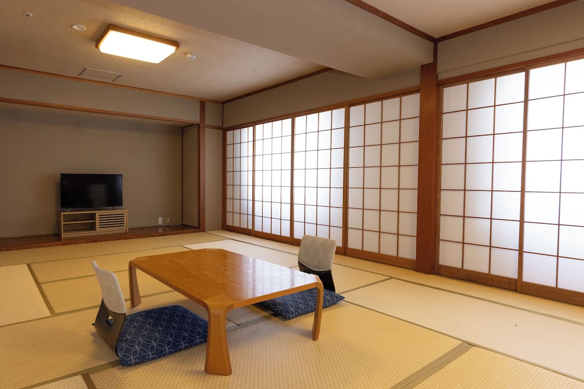 Una habitación japonesa tradicional con suelo de tatami, televisor, mesa de madera y puertas correderas shoji.