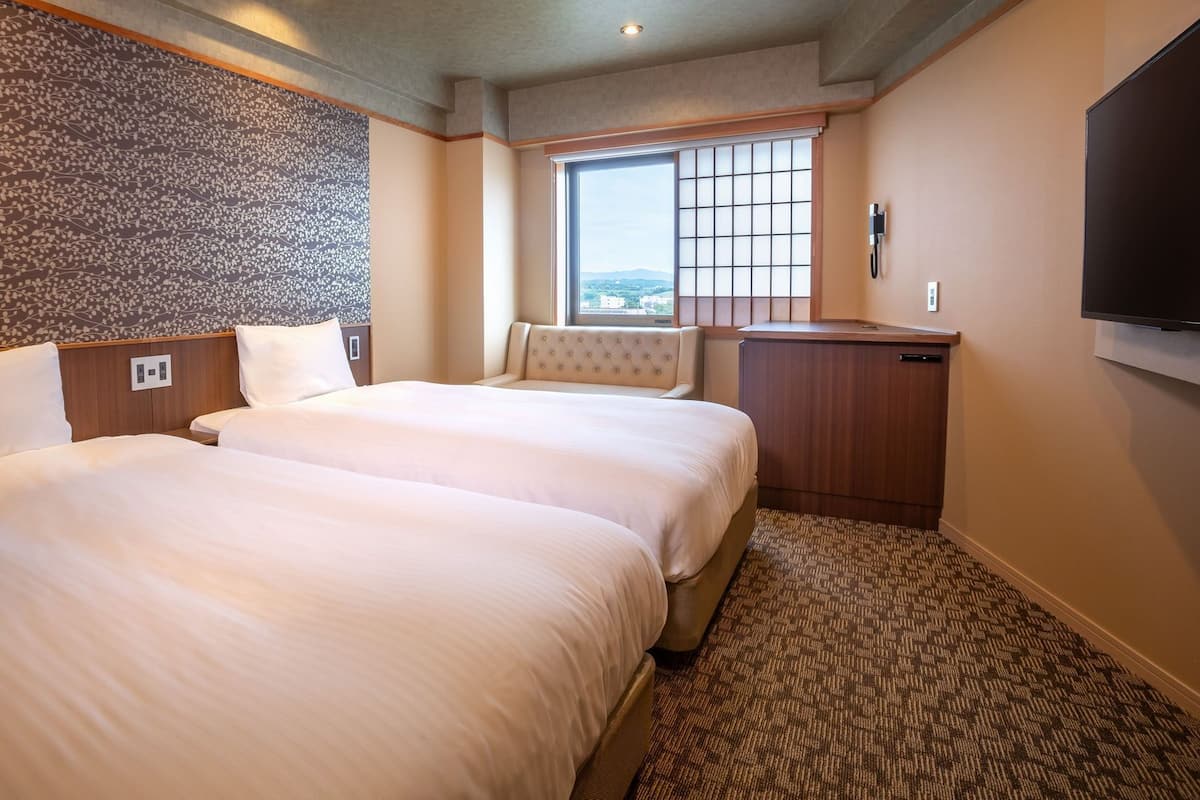 A hotel room with two beds, a window with a view, a flat-screen TV, and a minibar.