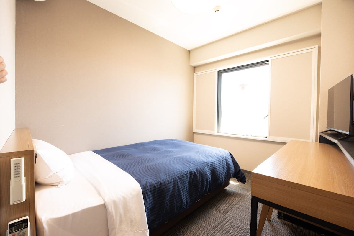 Una habitación de hotel con cama, escritorio, televisión y ventana.