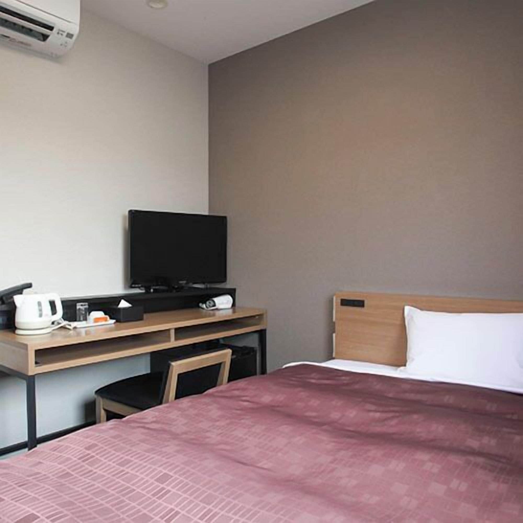 A hotel room with a bed, a television on a desk, and a coffee maker.
