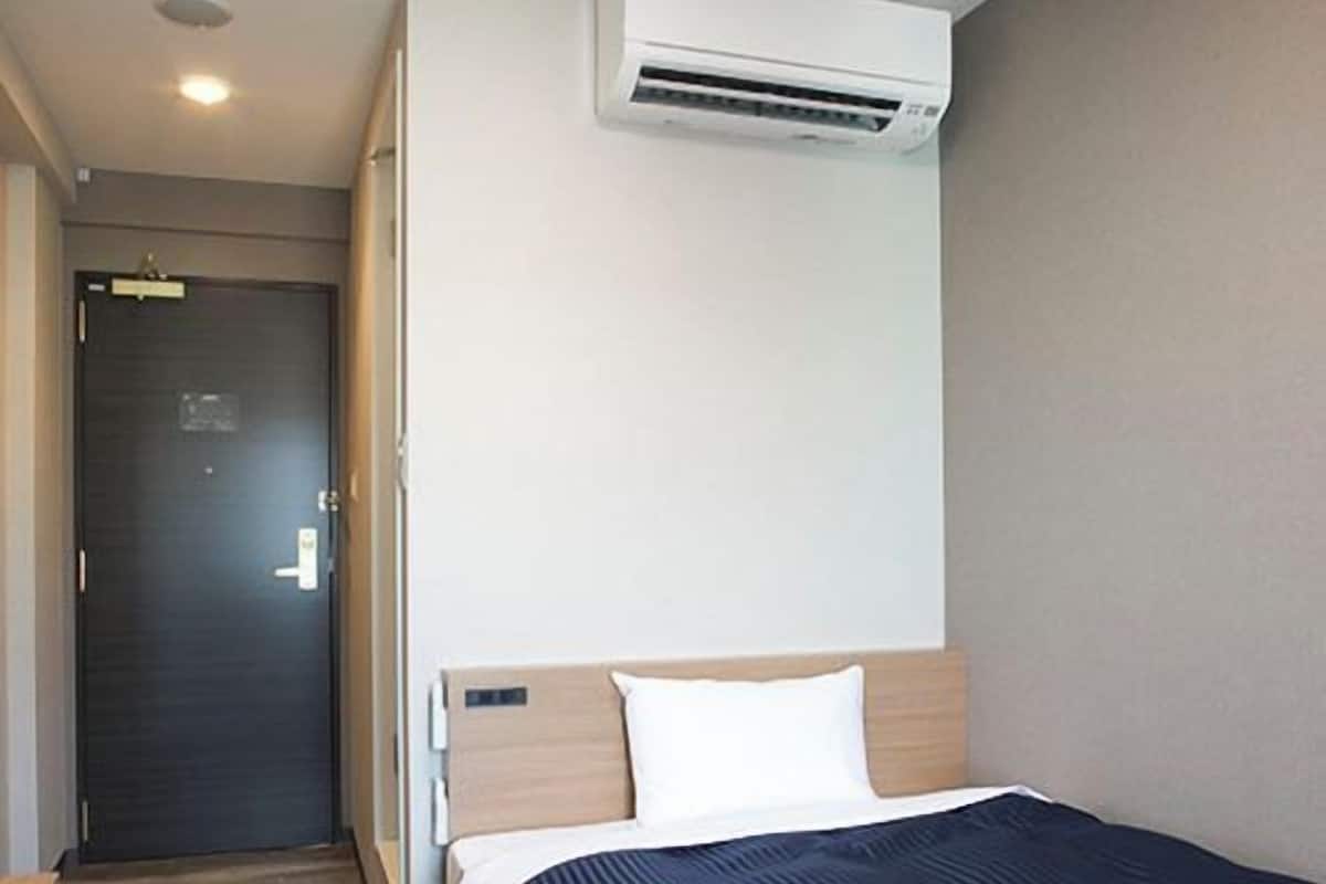 Una habitación de hotel con cama, escritorio, armario y aire acondicionado.