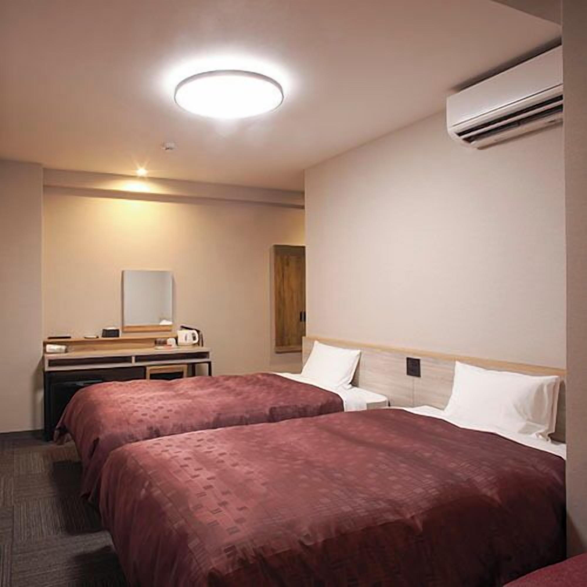 Habitación de hotel con dos camas, un escritorio con espejo y un equipo de aire acondicionado.