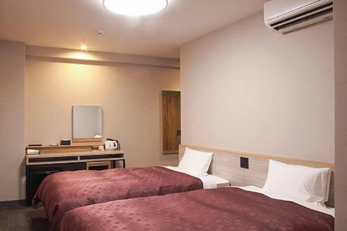 Habitación de hotel con dos camas, un escritorio con espejo y un equipo de aire acondicionado.