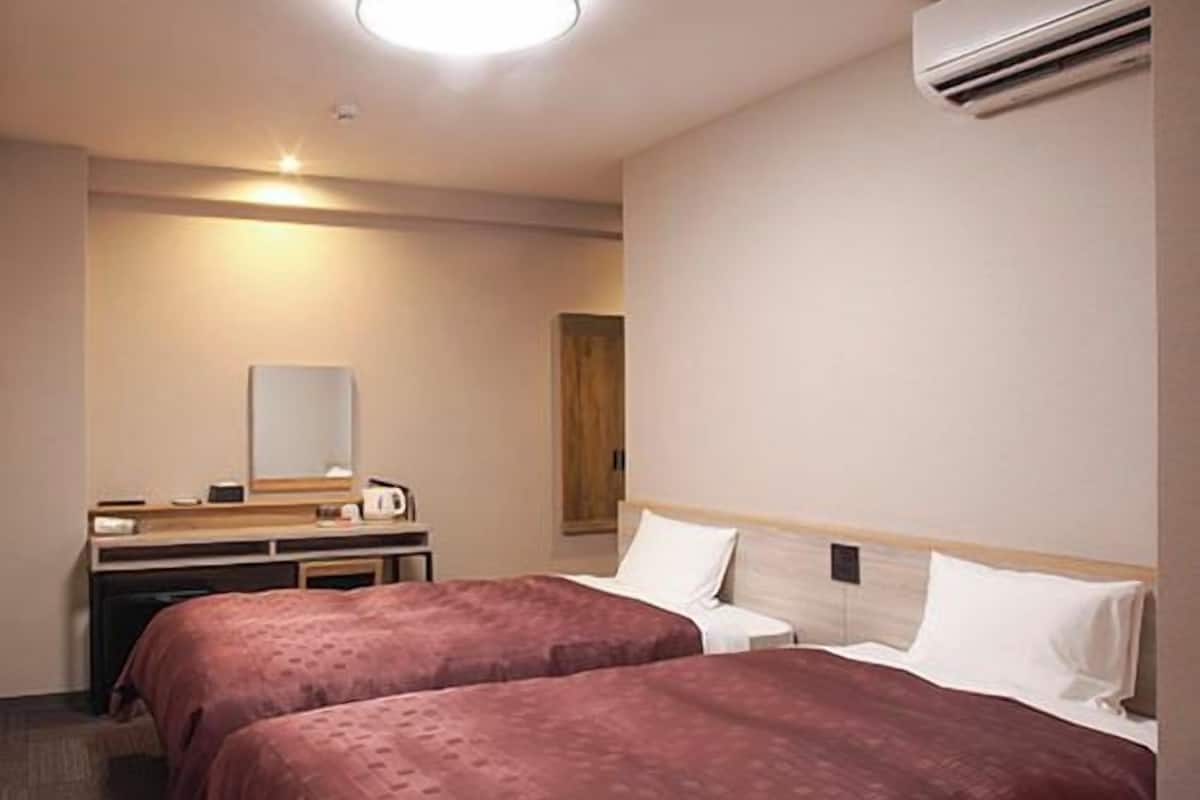 A hotel room with two beds, a desk with a mirror, and an air conditioning unit.