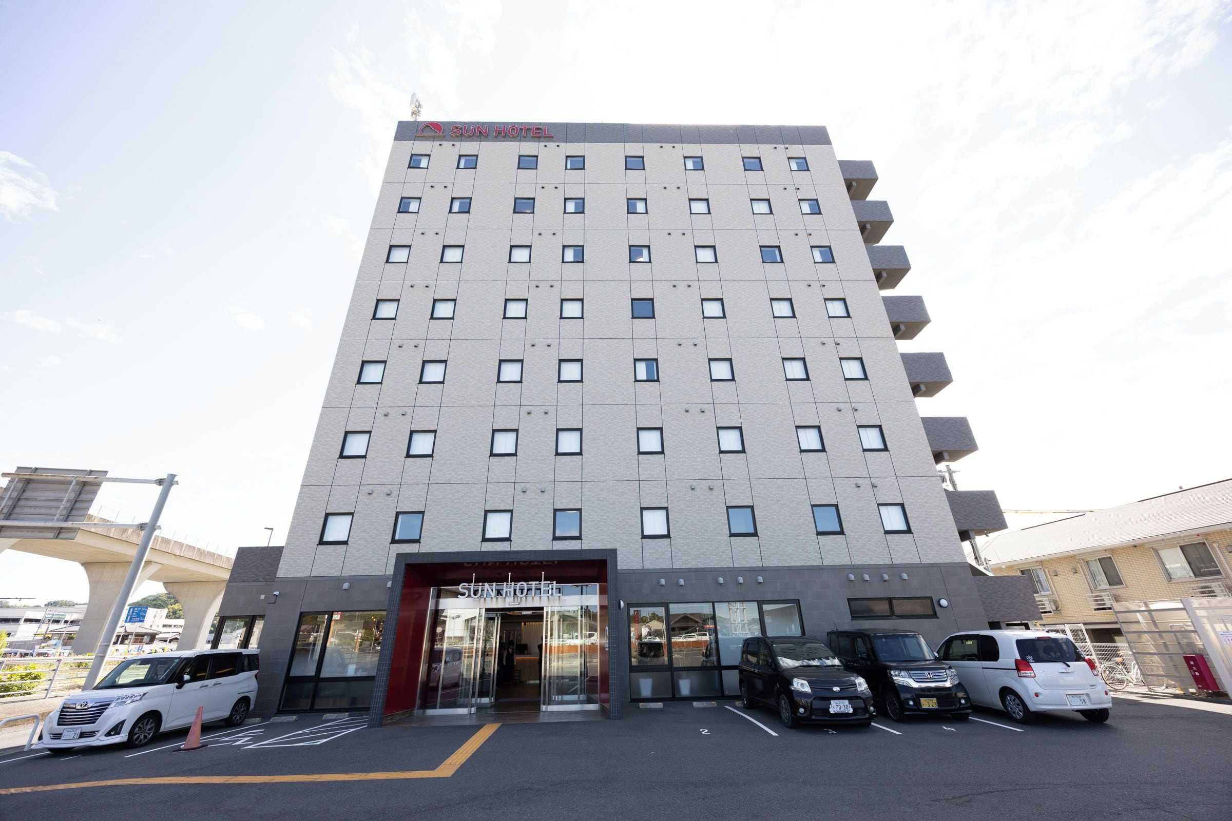 A multi-story hotel with a modern design, featuring a prominent entrance and a parking area in front.