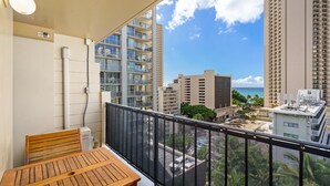 A balcony with a wooden table and a chair, overlooking a cityscape with tall buildings and a clear sky.