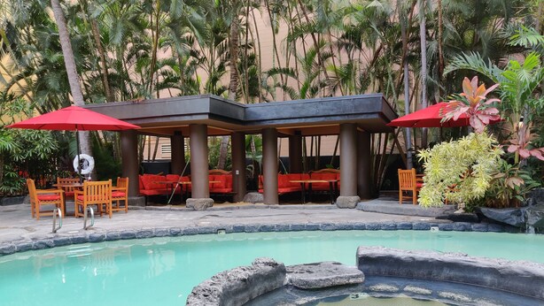 A pool area with a hot tub, red umbrellas, and seating under a covered area.