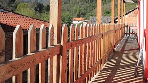 A wooden deck with a wooden railing, leading to a building with a red roof. - Auberge L'escaleta (Seix)