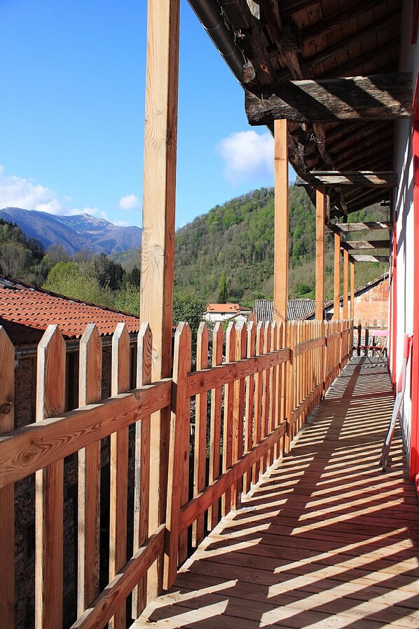 Una terraza de madera con barandilla de madera, que conduce a un edificio con techo rojo.