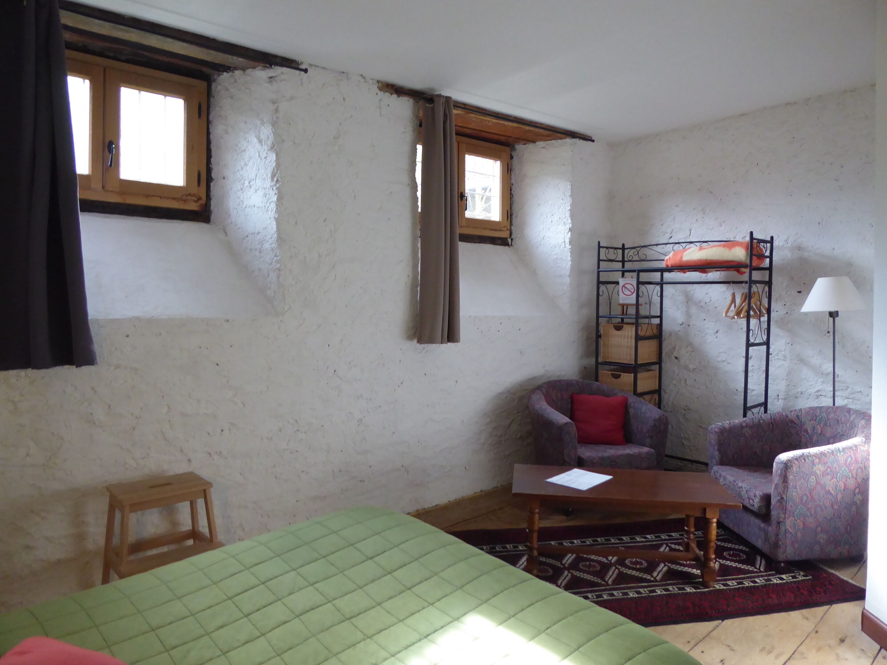 Una habitación con literas, dos sillas, una mesita y una cama con colcha verde.