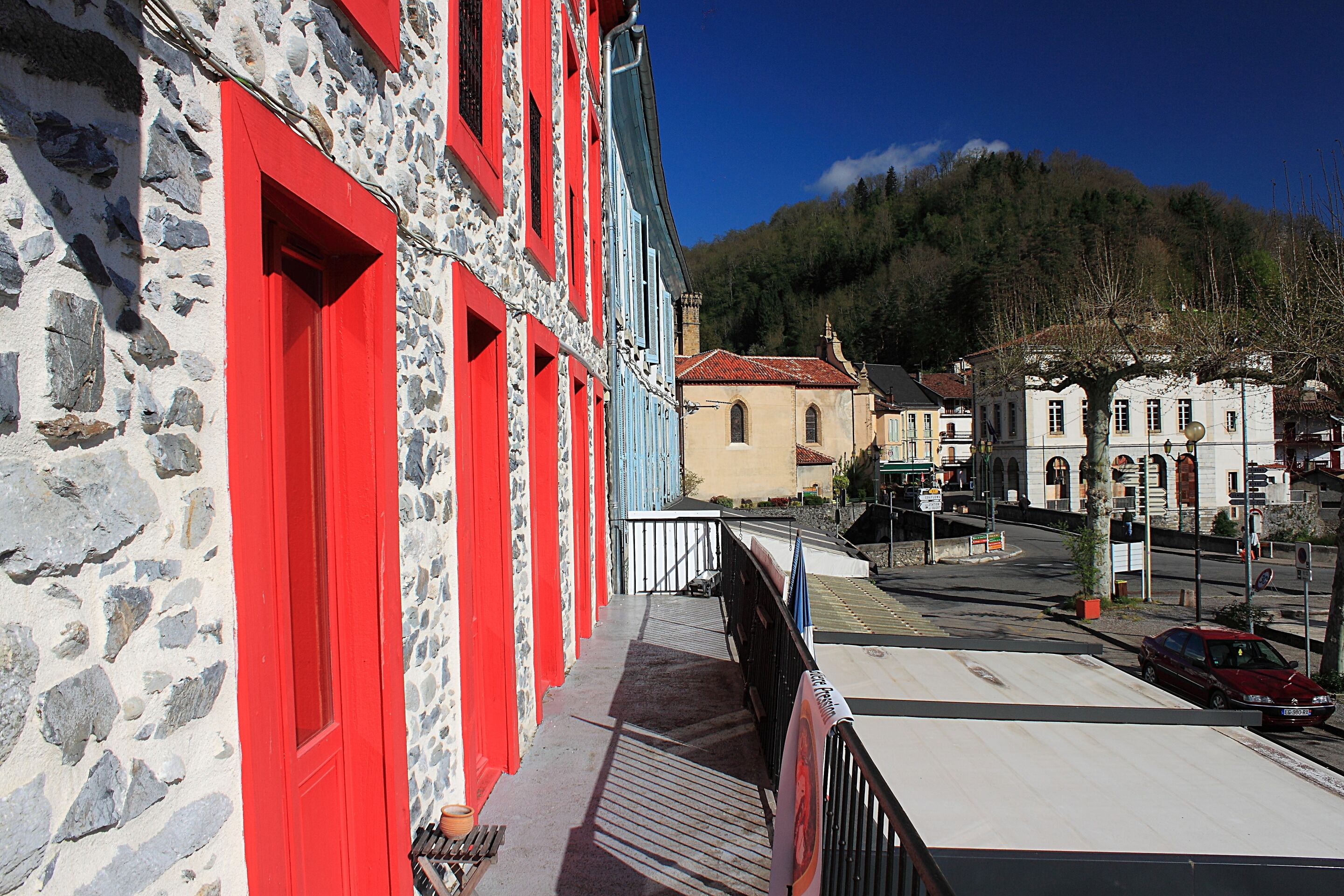 A stone building with red doors and windows, a paved street, and a mountain in the background.