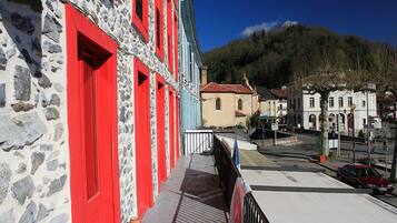 A stone building with red doors and windows, a paved street, and a mountain in the background.