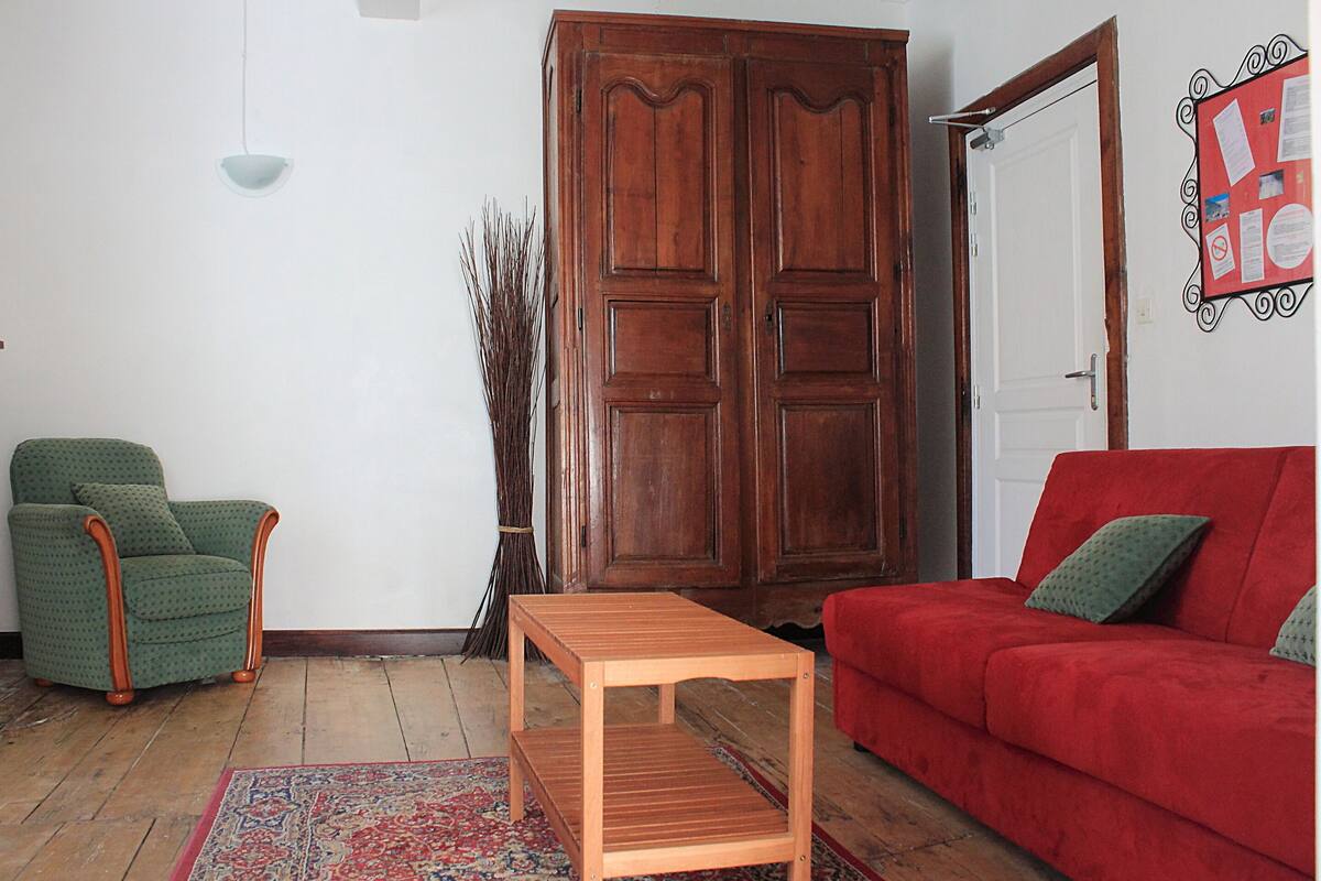 A living room with a wooden table, a red sofa, a green armchair, and a large wooden wardrobe.
