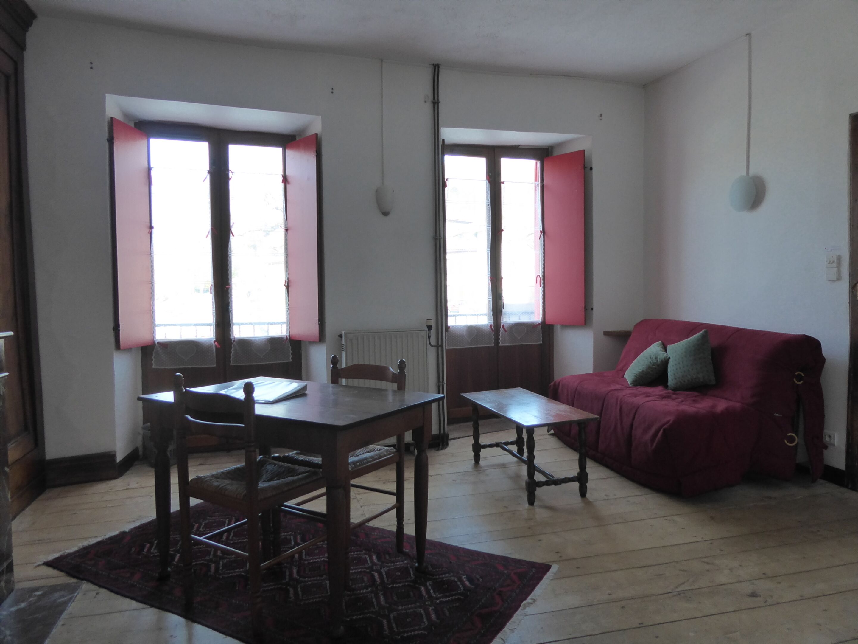 Una habitación con una mesa de comedor de madera, dos sillas, un sofá rojo y una alfombra estampada.