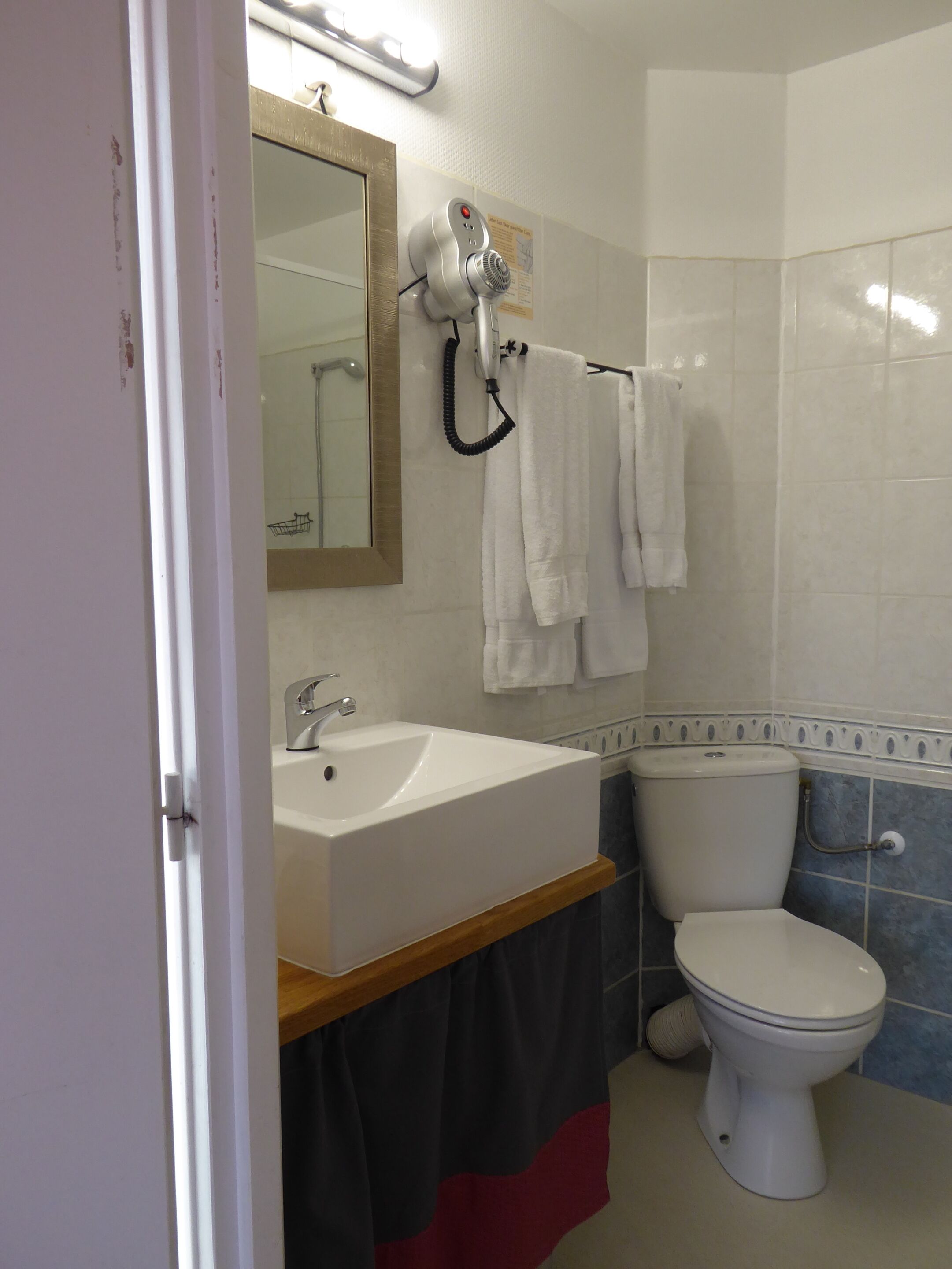 Een badkamer met een witte wastafel, een spiegel, een haardroger en een toilet.