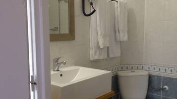 Een badkamer met een witte wastafel, een spiegel, een haardroger en een toilet.