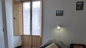 A bedroom with a bed, a nightstand, a wall-mounted lamp, a door with a view, and a small picture on the wall. - Auberge L'escaleta (Seix)