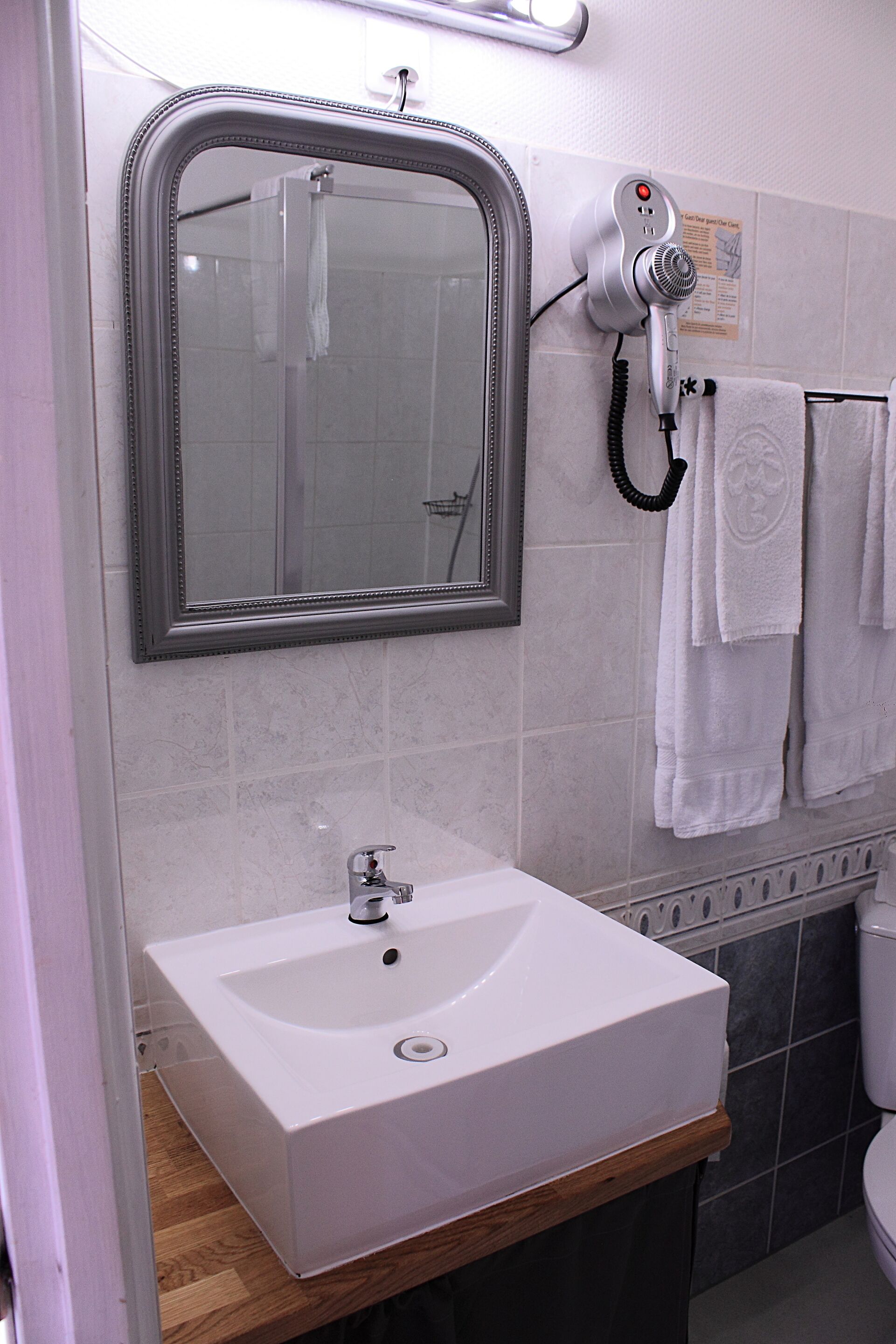A bathroom with a white sink, a mirror, and a hairdryer mounted on the wall.