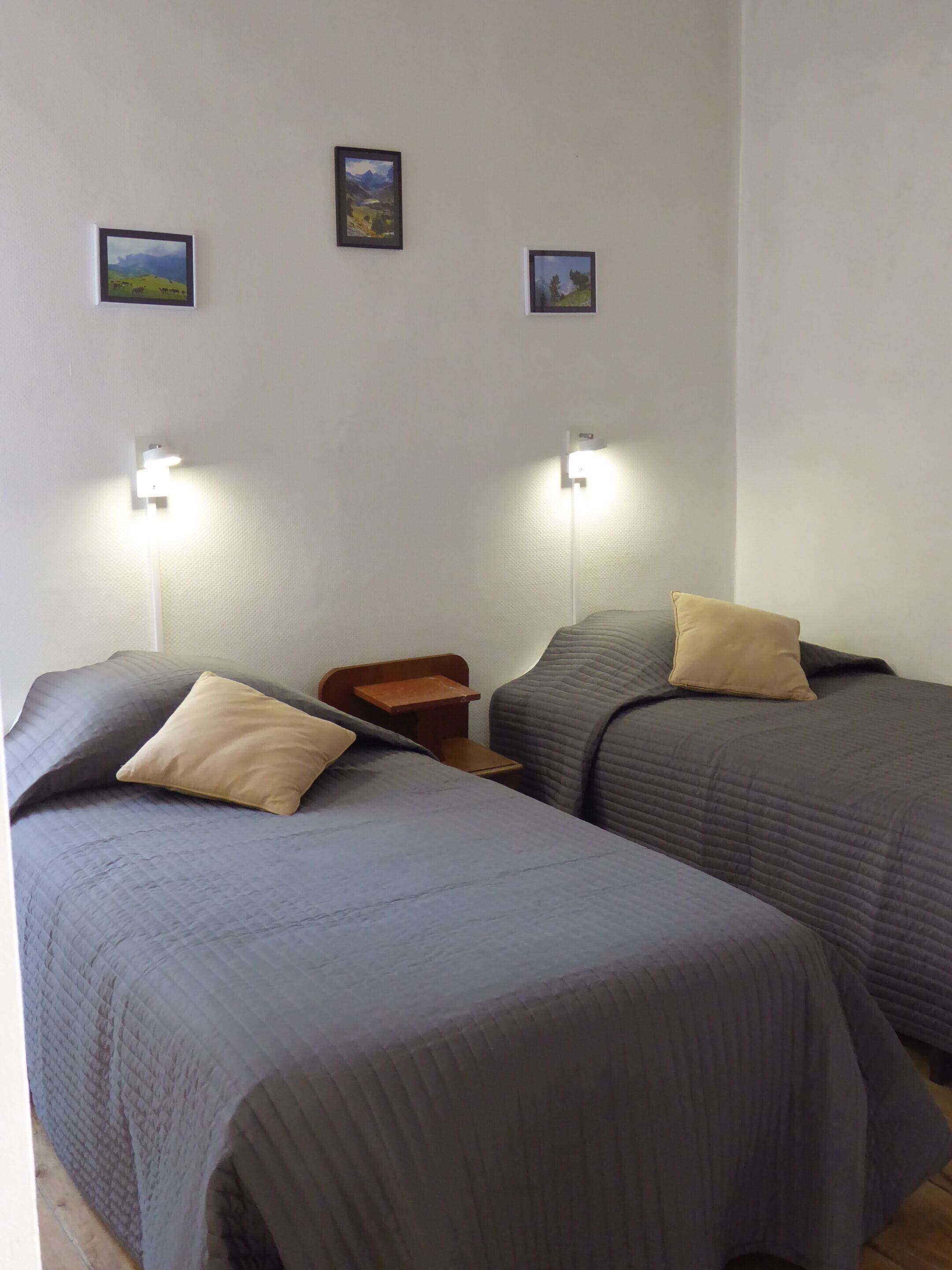 A room with two beds, each with a pillow and a nightstand. There are wall-mounted lights above the beds.