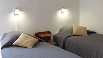 A room with two beds, each with a pillow and a nightstand. There are wall-mounted lights above the beds.
