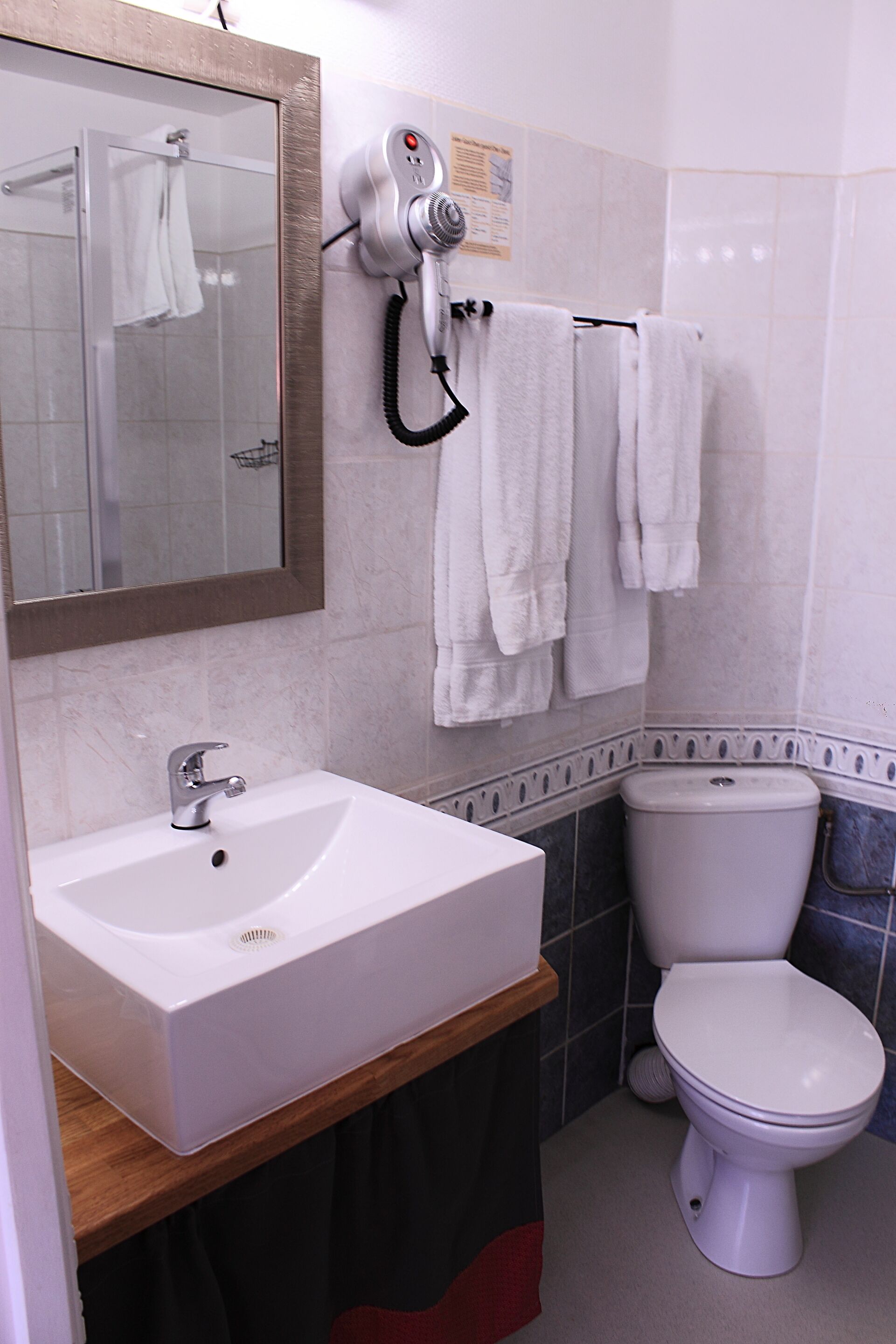 A bathroom with a white sink, a mirror, a toilet, and a hairdryer mounted on the wall.
