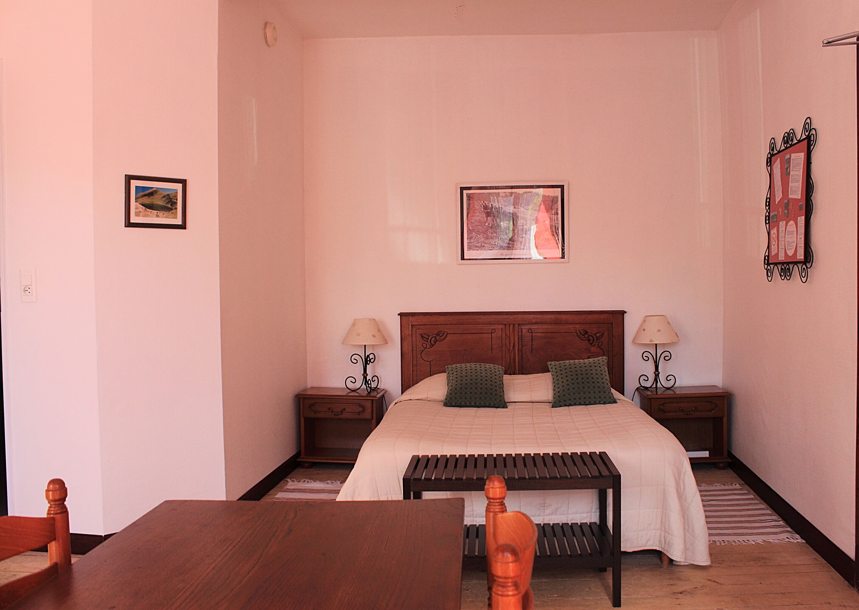 Une chambre à coucher avec un lit en bois, deux tables de chevet avec des lampes, un banc en bois et un tableau encadré au mur.
