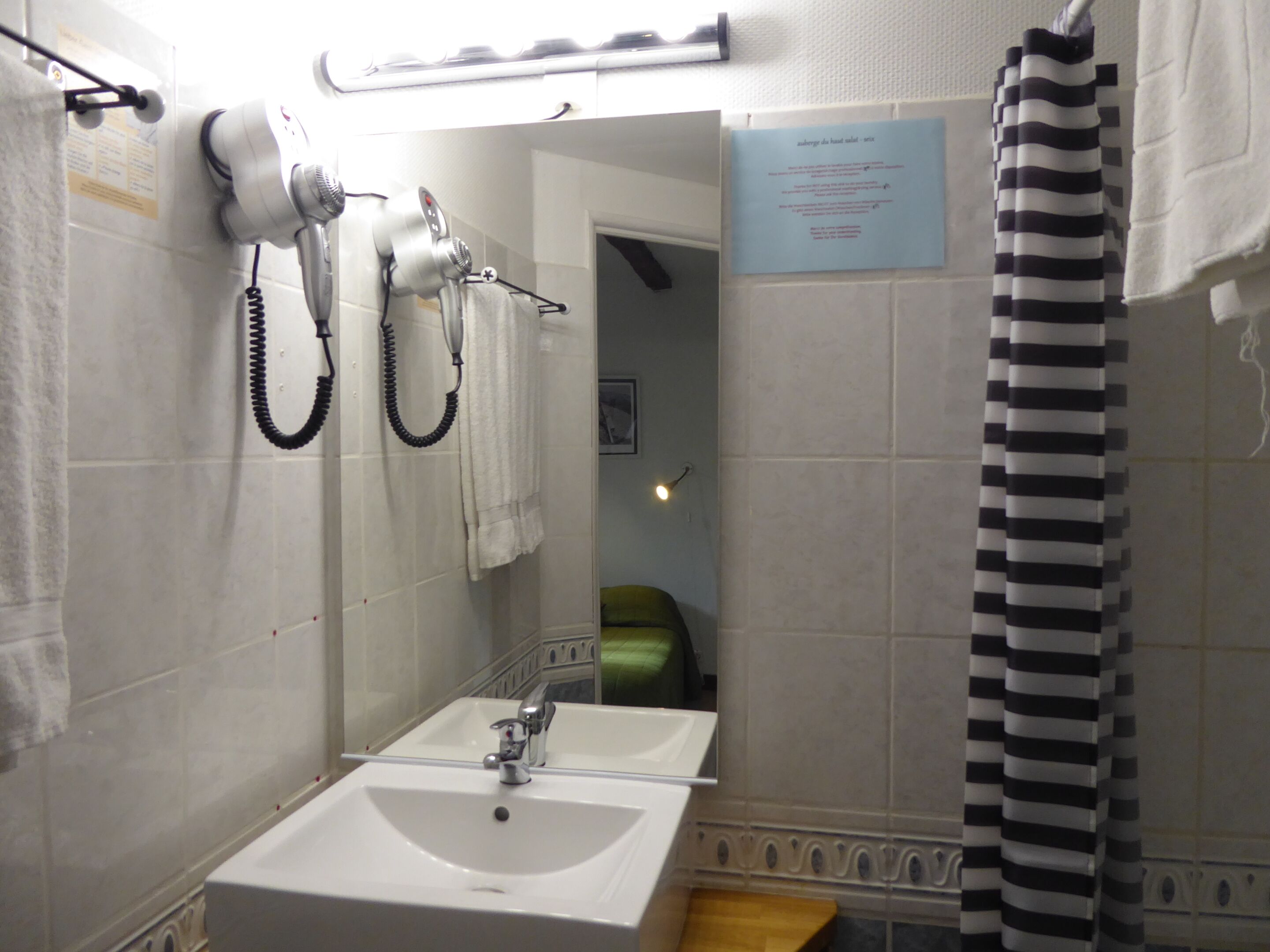Ein Badezimmer mit Waschbecken, Spiegel und zwei an der Wand befestigten Haartrocknern.