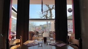A restaurant with a table set for two, a hanging heart decoration, and a view of the street outside. - Auberge L'escaleta (Seix)