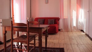 A room with a wooden dining table and chairs, a red sofa with patterned cushions, and a radiator. - Auberge L'escaleta (Seix)