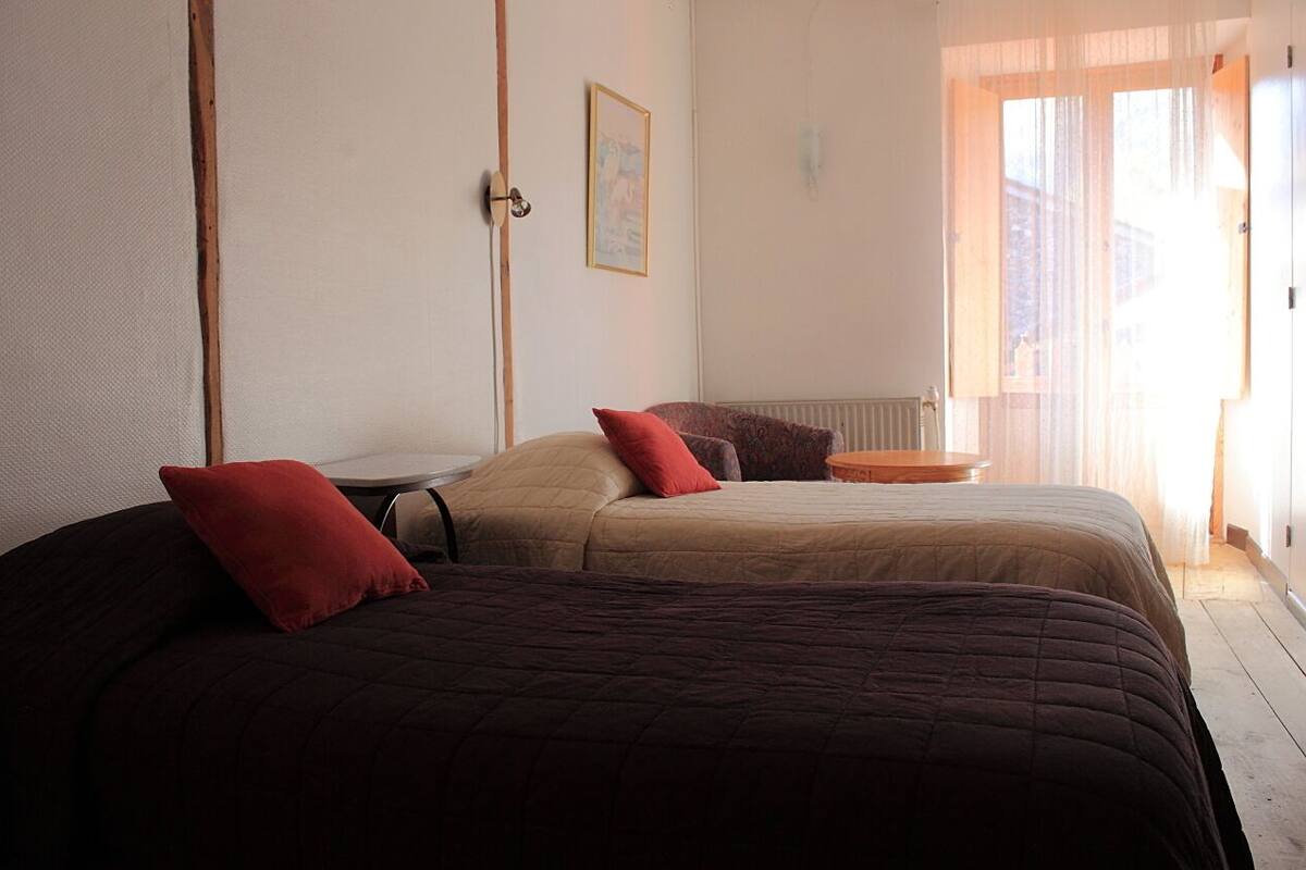 A bedroom with two beds, a small table, and a window with curtains.