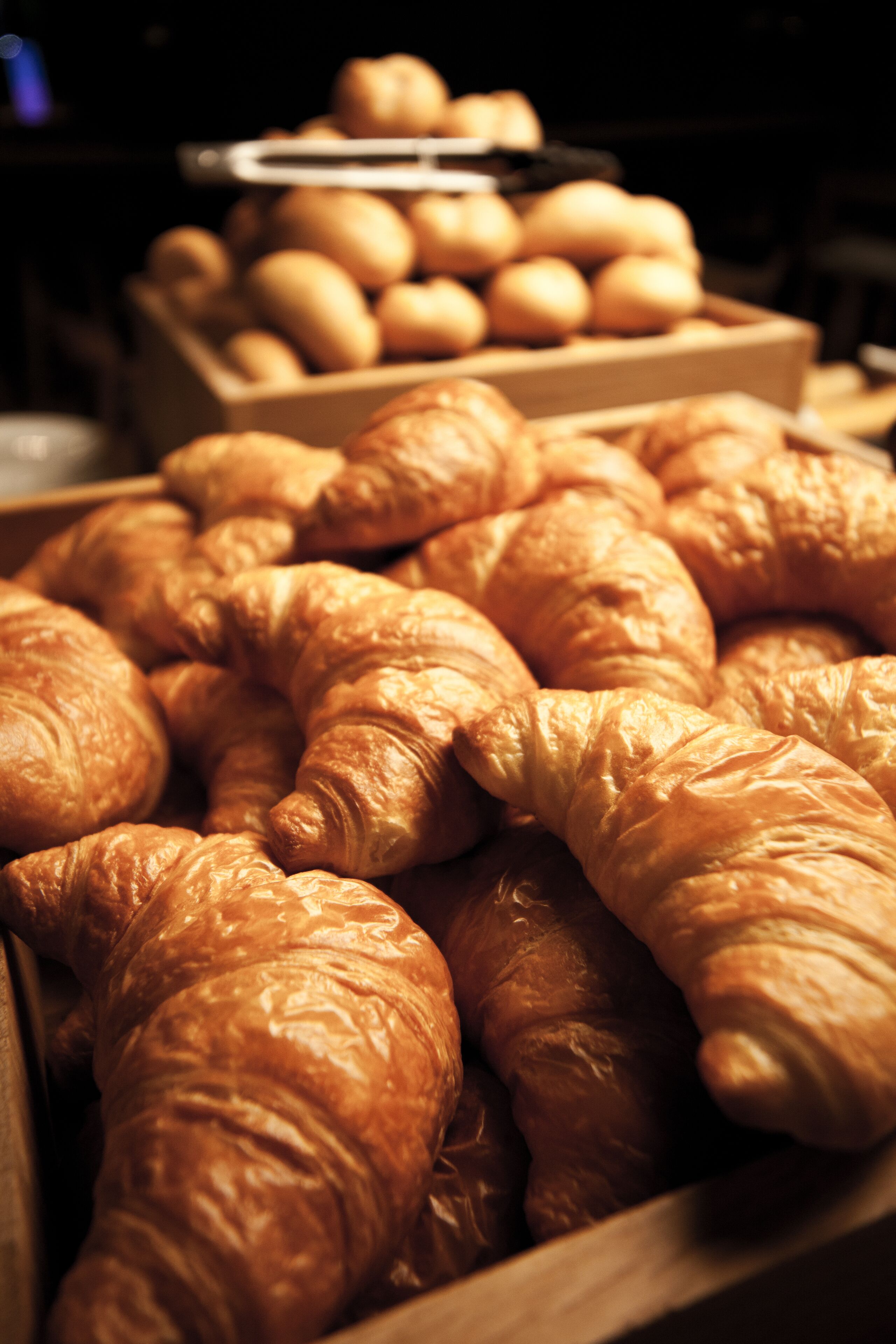 A display of golden-brown croissants and potatoes in wooden crates.