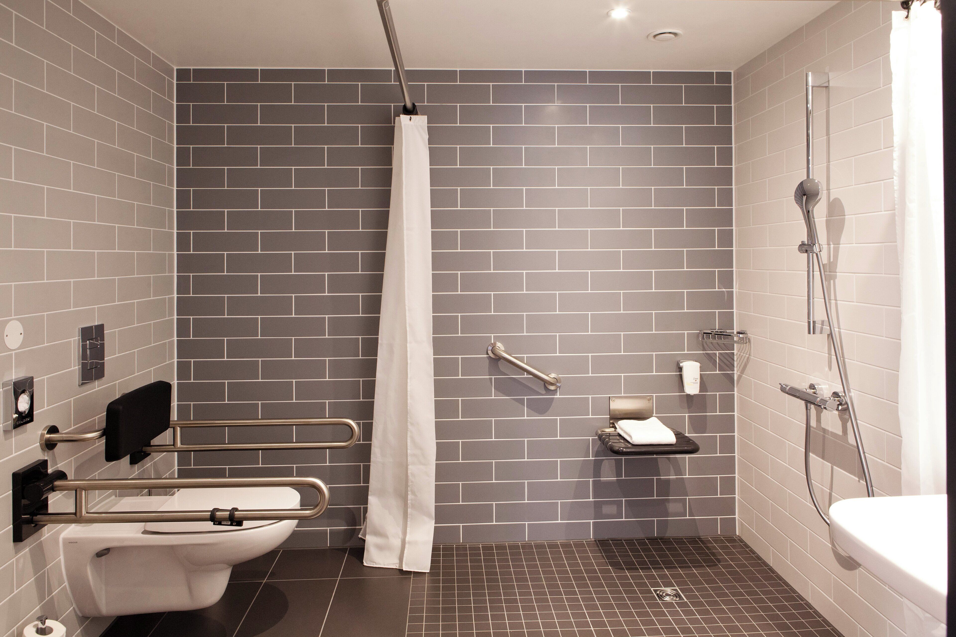 Un baño moderno con ducha, inodoro y barras de apoyo.
