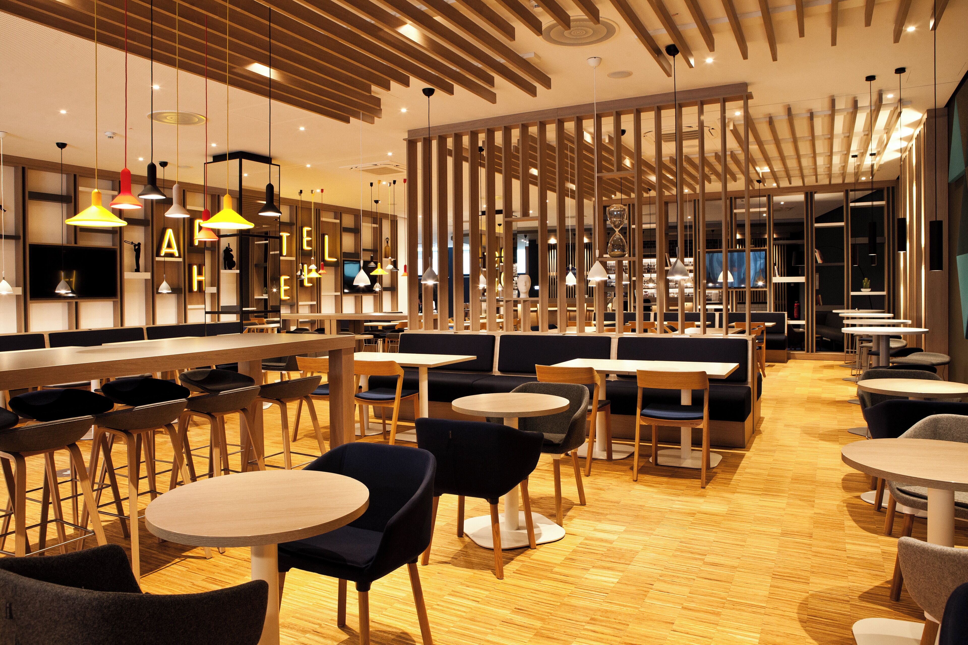 A modern restaurant interior with wooden flooring, round tables, and black and grey chairs.
