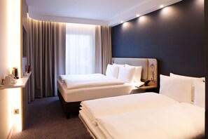A hotel room with two beds, a desk with a lamp, and a large window with curtains.